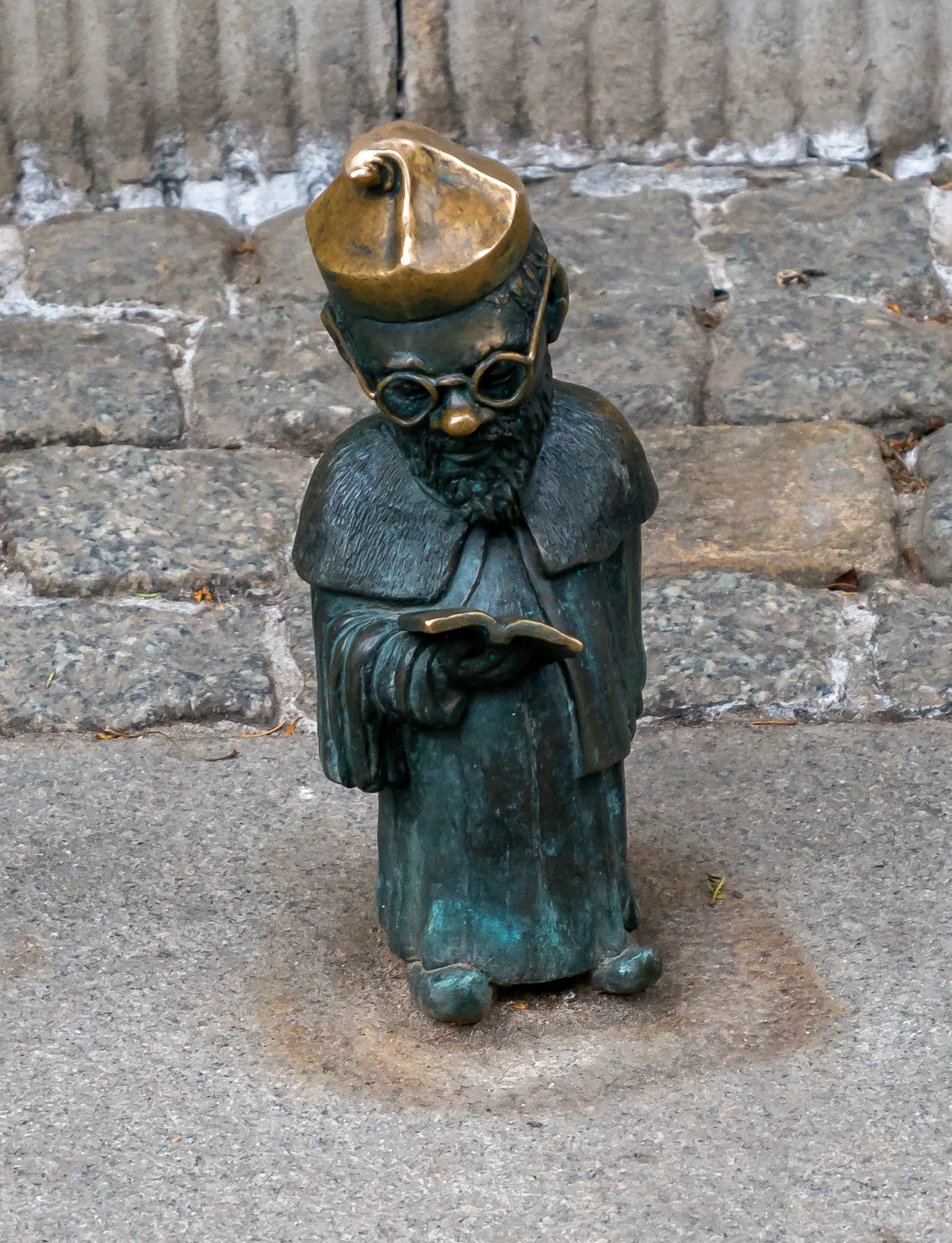 Un petit nain en bronze en train de lire sur la place de l’Université à Wrocław.